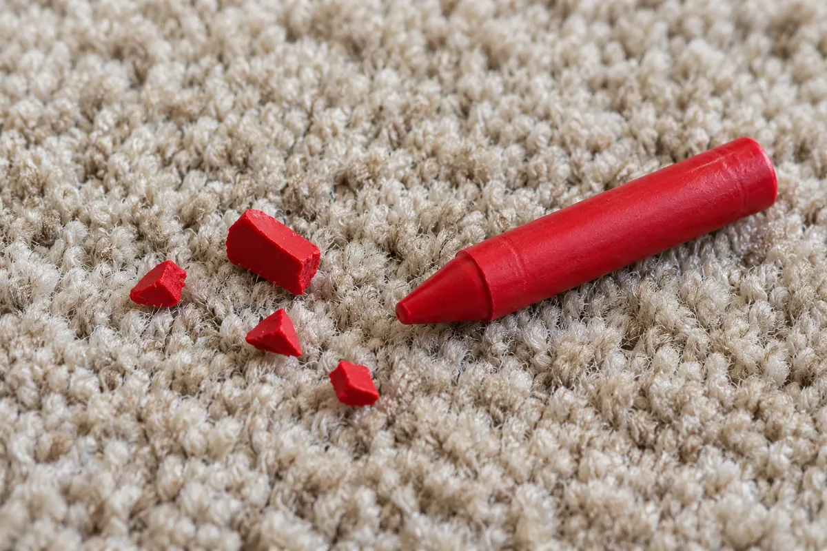 Loose red crayon fragments resting on beige carpet beside a red crayon.